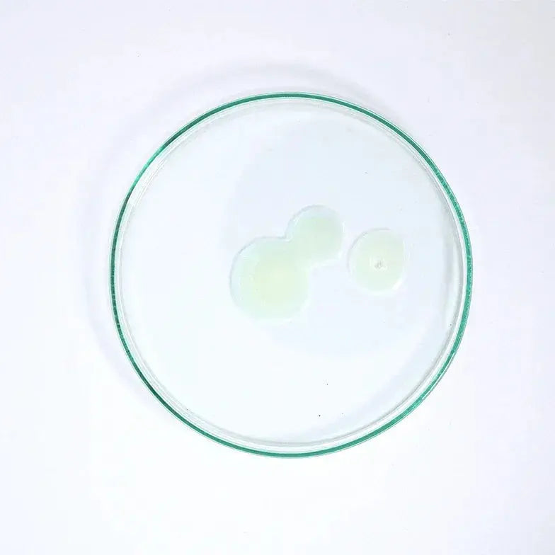Clear and light green skincare serum swatch on glass dish, isolated on white background