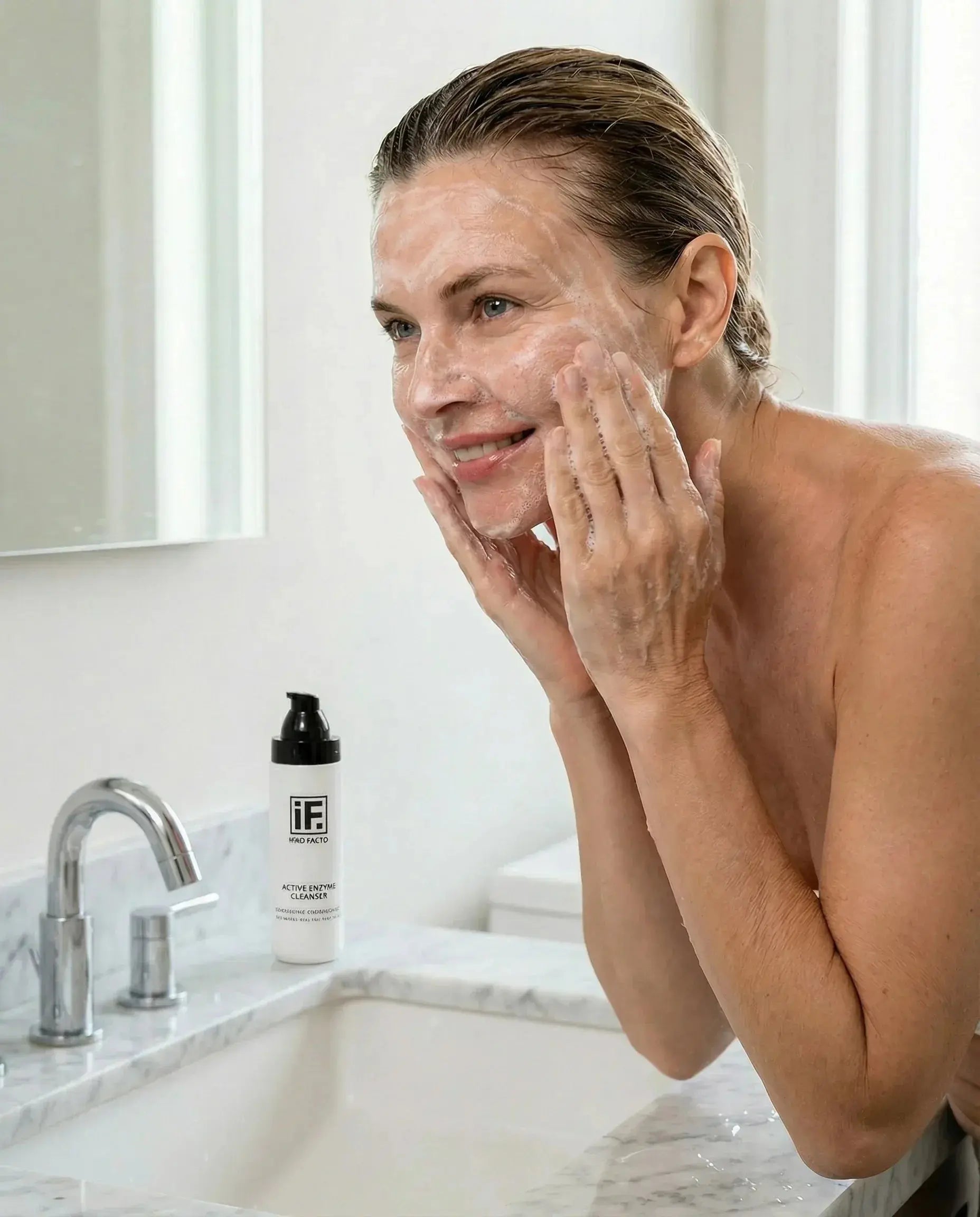Woman gently cleansing face with foaming enzyme cleanser at bathroom sink