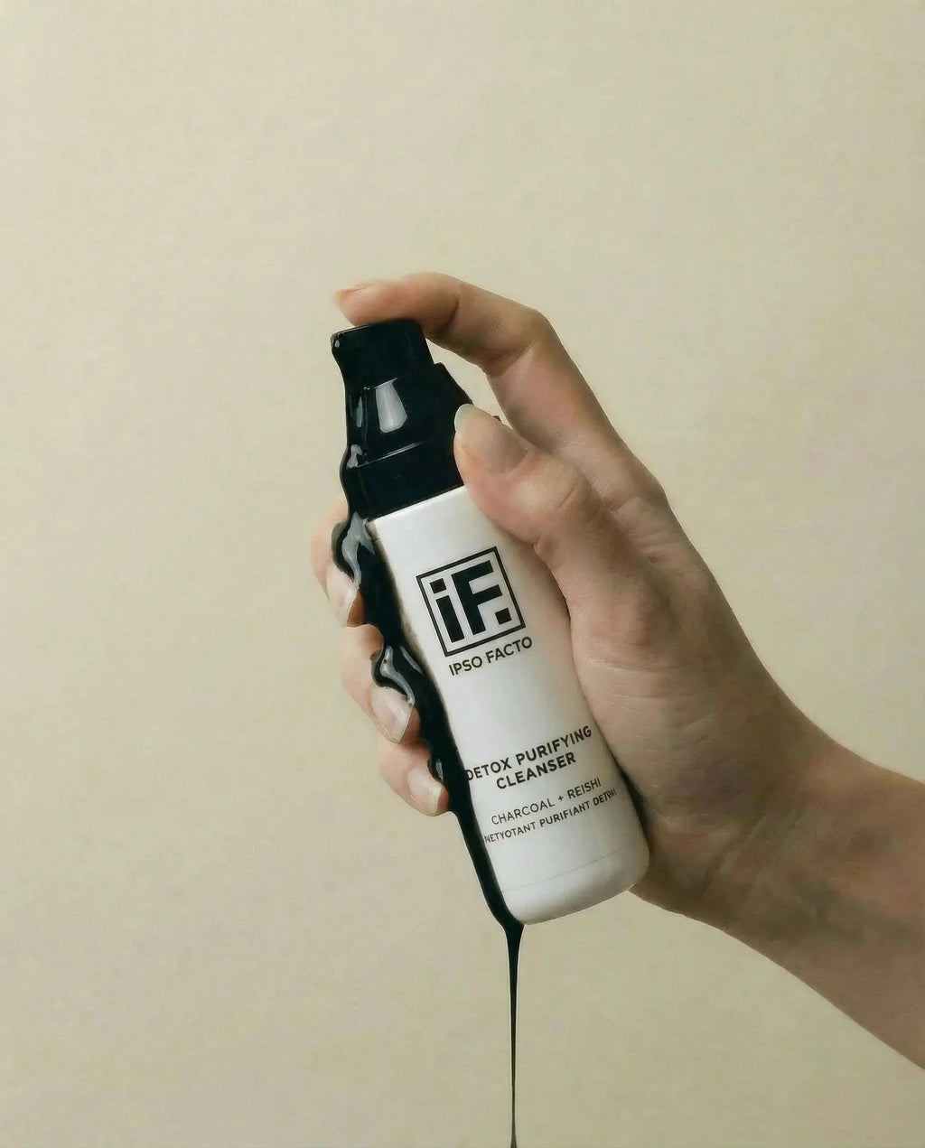 Hand holding a detox purifying cleanser bottle with black charcoal liquid flowing down