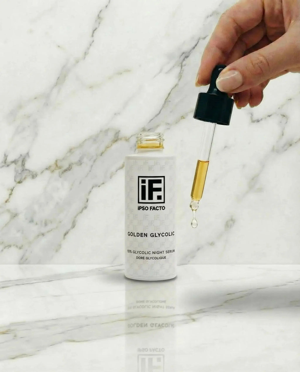 Hand holding dropper above Golden Glycolic night serum bottle on marble surface