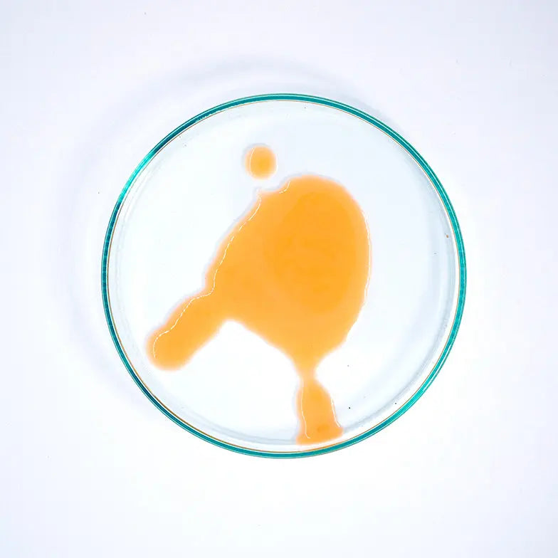Turmeric serum swatch in a glass dish on white background, natural skincare product